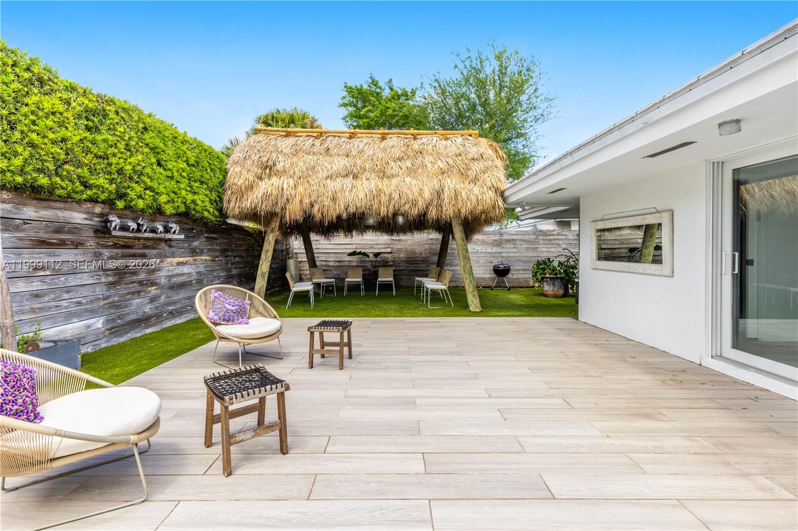 A backyard patio features light-colored tile flooring, a thatched-roof tiki hut, and outdoor seating — 524 Warren Ln, Key Biscayne FL 33149, KEY BISCAYNE, FL