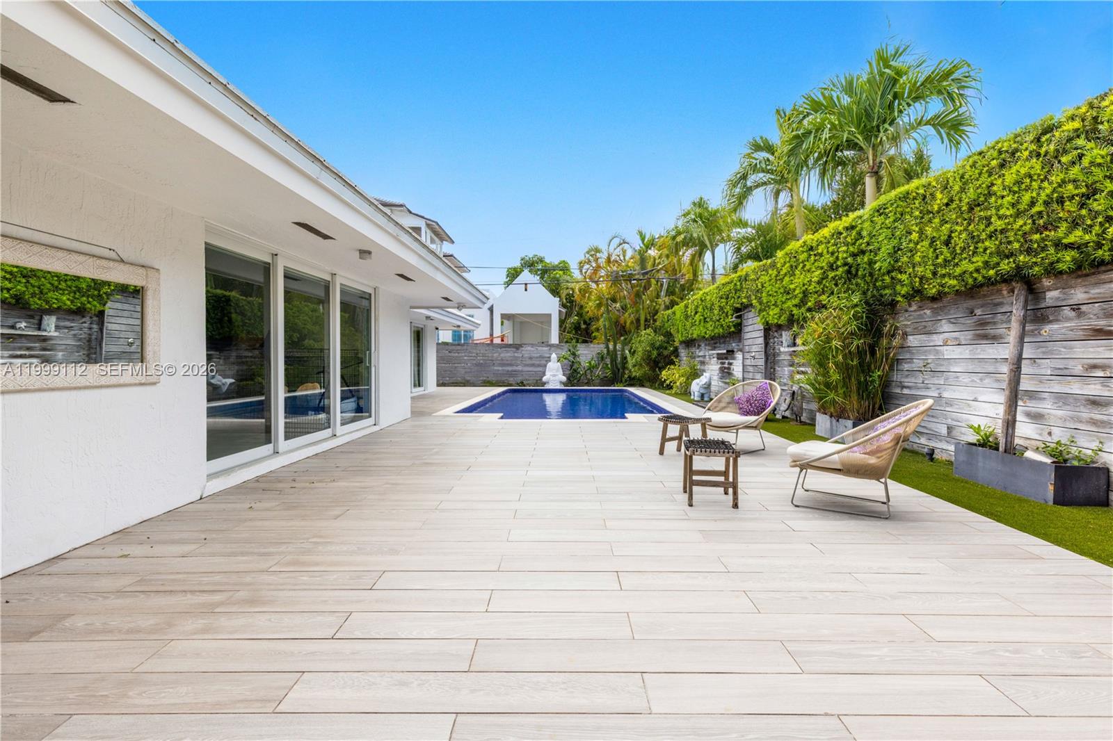 A backyard patio features light-colored tile flooring, a rectangular swimming pool, and outdoor seating — 524 Warren Ln, Key Biscayne FL 33149, KEY BISCAYNE, FL