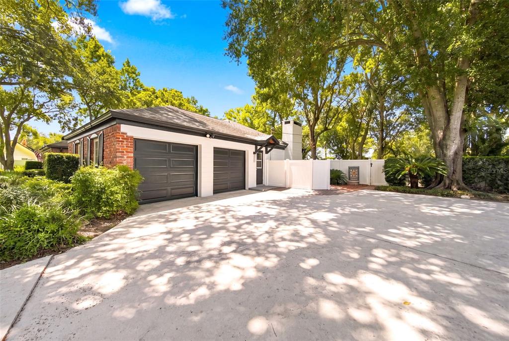 A detached two-car garage with brick accents sits beside a white fence and trees — 211 TALMEDA TRAIL, MAITLAND, FL