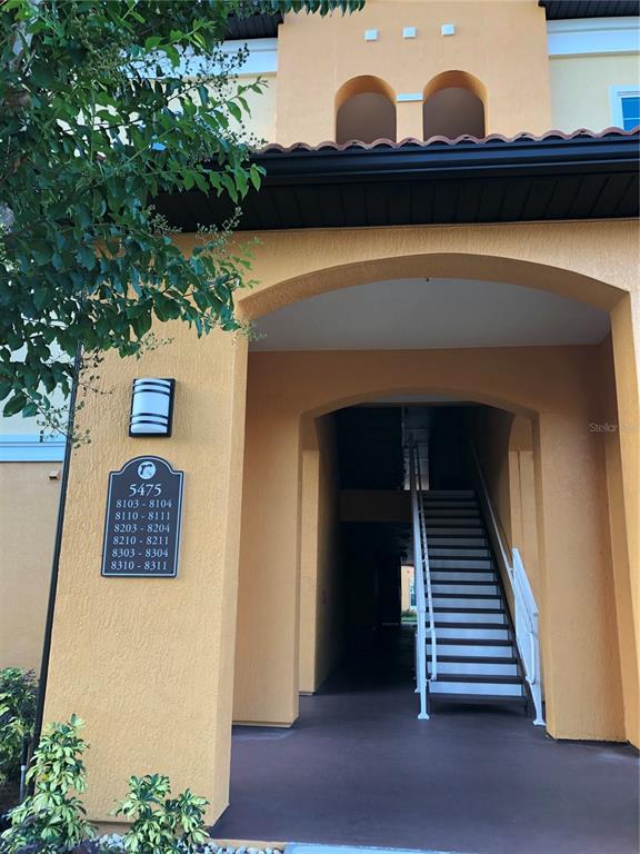 An exterior view of an apartment building entrance with a staircase and unit number sign — 5475 VINELAND ROAD UNIT 8304, ORLANDO, FL