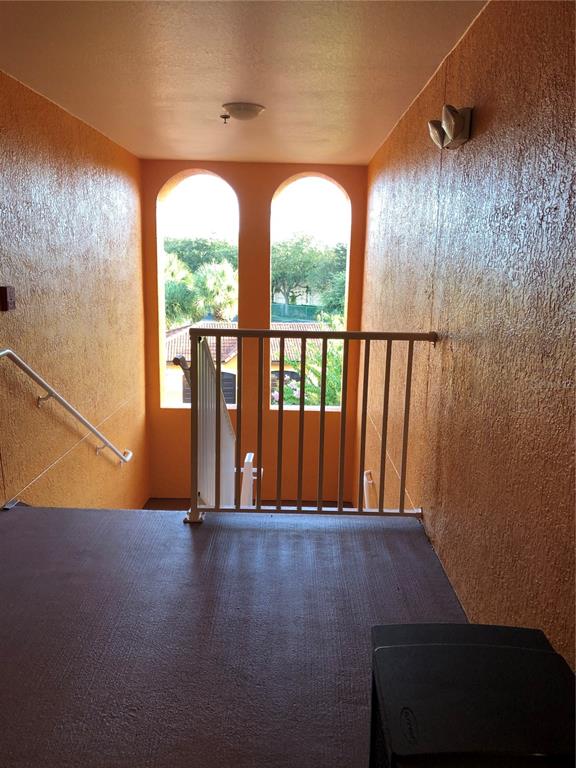 An outdoor stairwell landing with orange textured walls, a white metal railing, and arched windows — 5475 VINELAND ROAD UNIT 8304, ORLANDO, FL