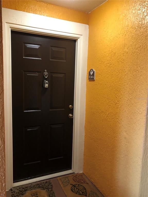 A dark brown door with a lockbox and a unit number sign on a yellow wall — 5475 VINELAND ROAD UNIT 8304, ORLANDO, FL