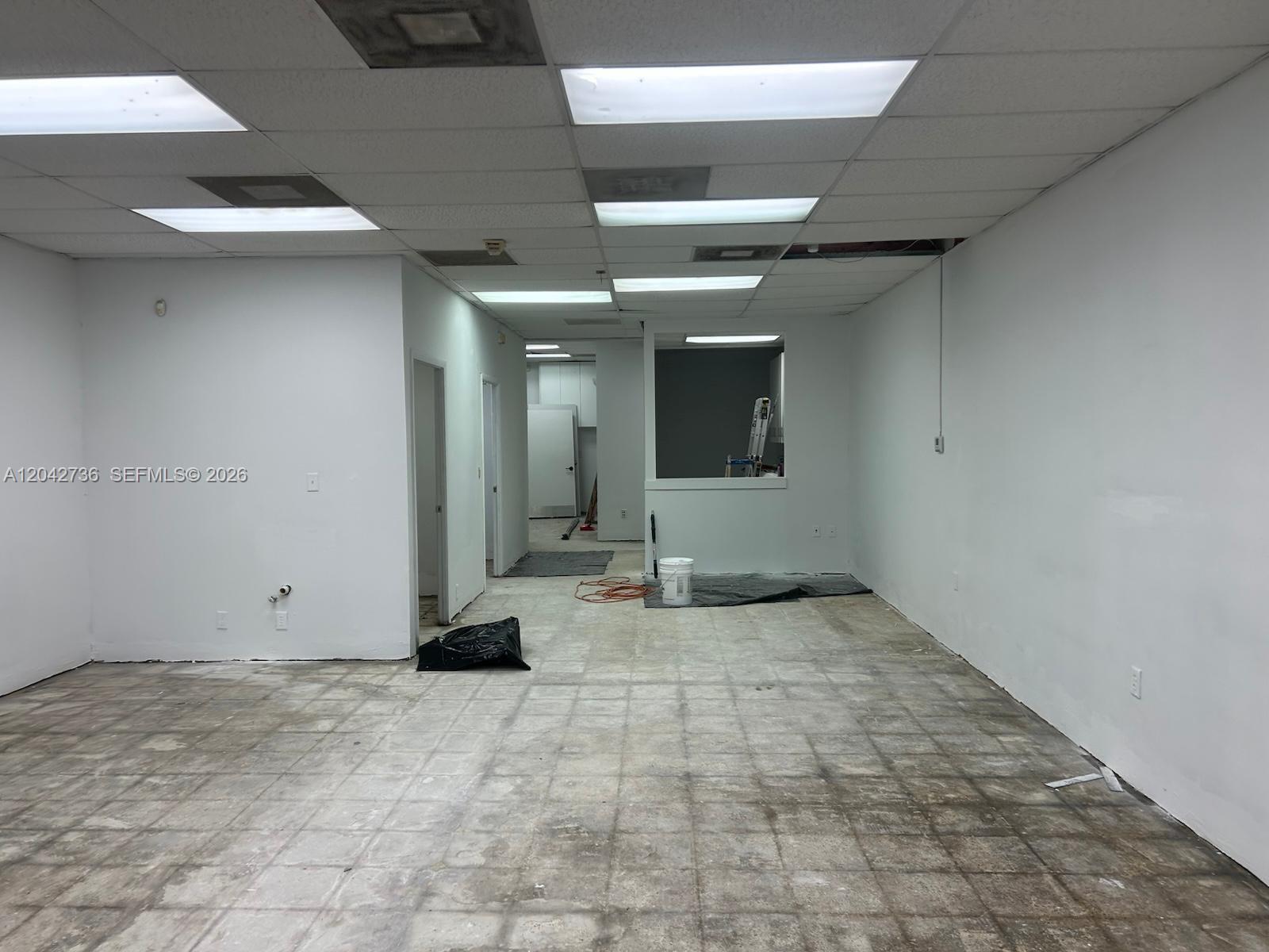 An empty commercial space features a drop ceiling, white walls, and worn tiled flooring — 9360 NW 27th Ave, Miami FL 33147, MIAMI, FL