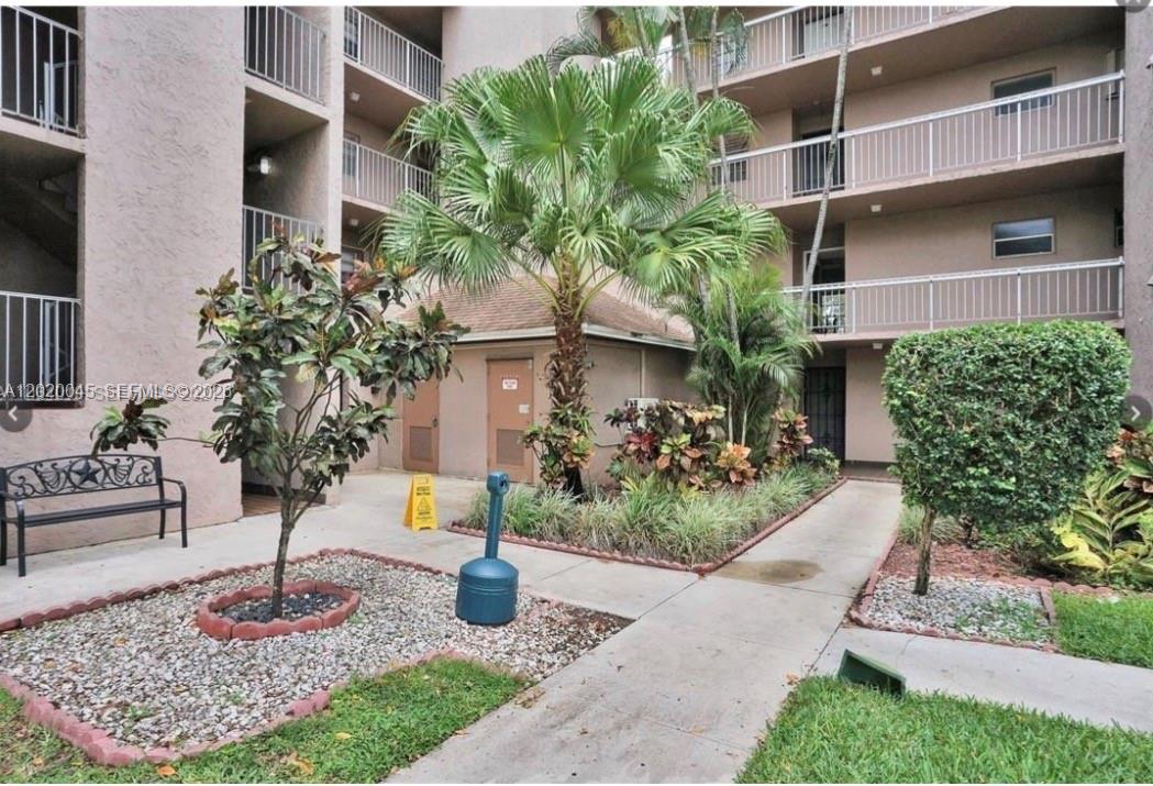 A courtyard with a palm tree, landscaping, a bench, and a multi-story apartment building — 9480 Tangerine Pl # 404, Davie FL 33324, DAVIE, FL