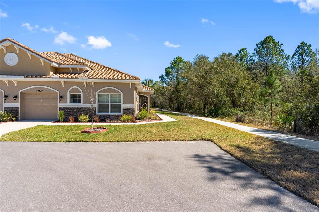 A tan house with a tiled roof and a paved walkway next to a wooded area — 29800 ANAND VIHAR DRIVE, WESLEY CHAPEL, FL