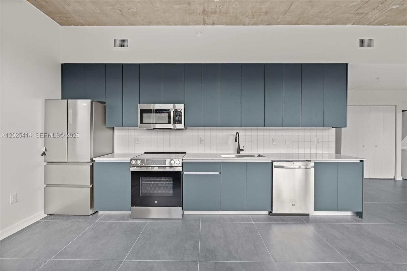 A modern kitchen features blue flat-panel cabinets, stainless steel appliances, and gray tile flooring — 315 NW 32 ST # 301, Miami FL 33127, MIAMI, FL