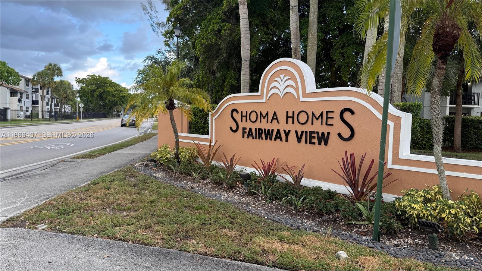 A tan monument sign for Shoma Homes Fairway View stands beside a road and palm trees — 17720 NW 73rd Ave # 105, Hialeah FL 33015, HIALEAH, FL