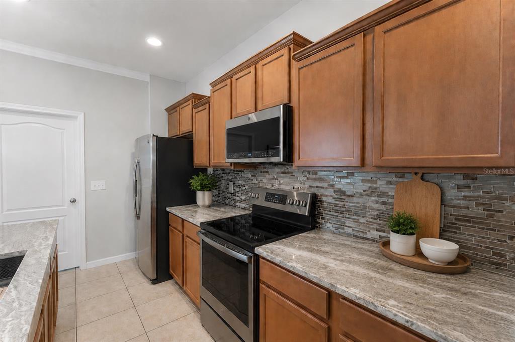 A kitchen features wood cabinets, stainless steel appliances, and a stone-look countertop — 9143 SAVANNAH AINSLEY LANE, ORLANDO, FL