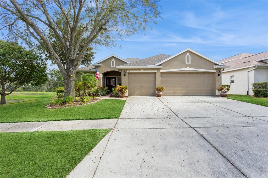 A single-story house features a three-car garage, a concrete driveway, and a large front tree — 1433 EMERALD HILL WAY, VALRICO, FL