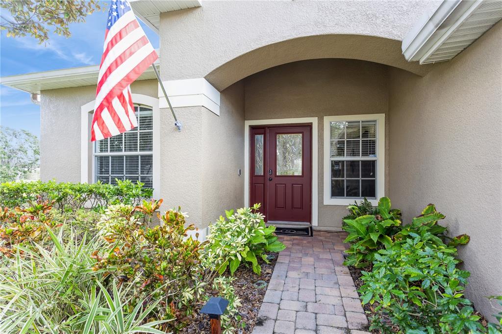 The exterior of a house features a red front door, a stone walkway, and landscaping — 1433 EMERALD HILL WAY, VALRICO, FL