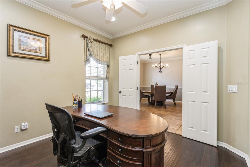 A home office with a wooden desk and chair, featuring double doors opening to a dining room — 1433 EMERALD HILL WAY, VALRICO, FL