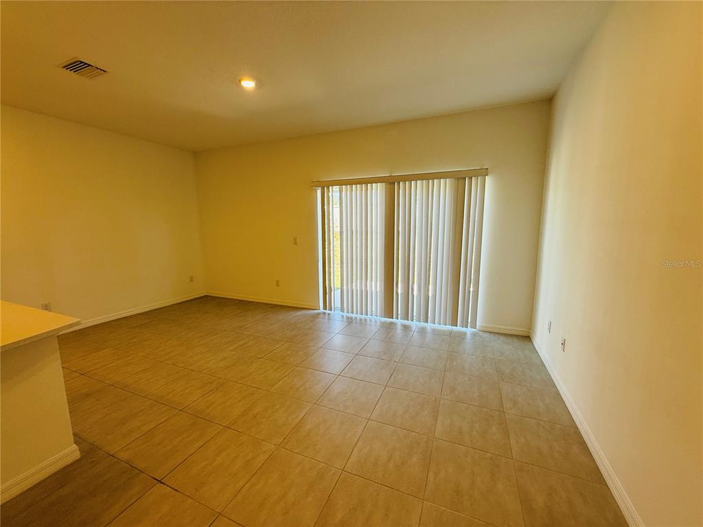 An empty room with beige tile flooring and vertical blinds covering a sliding glass door — 2264 PARAVANE WAY, WESLEY CHAPEL, FL