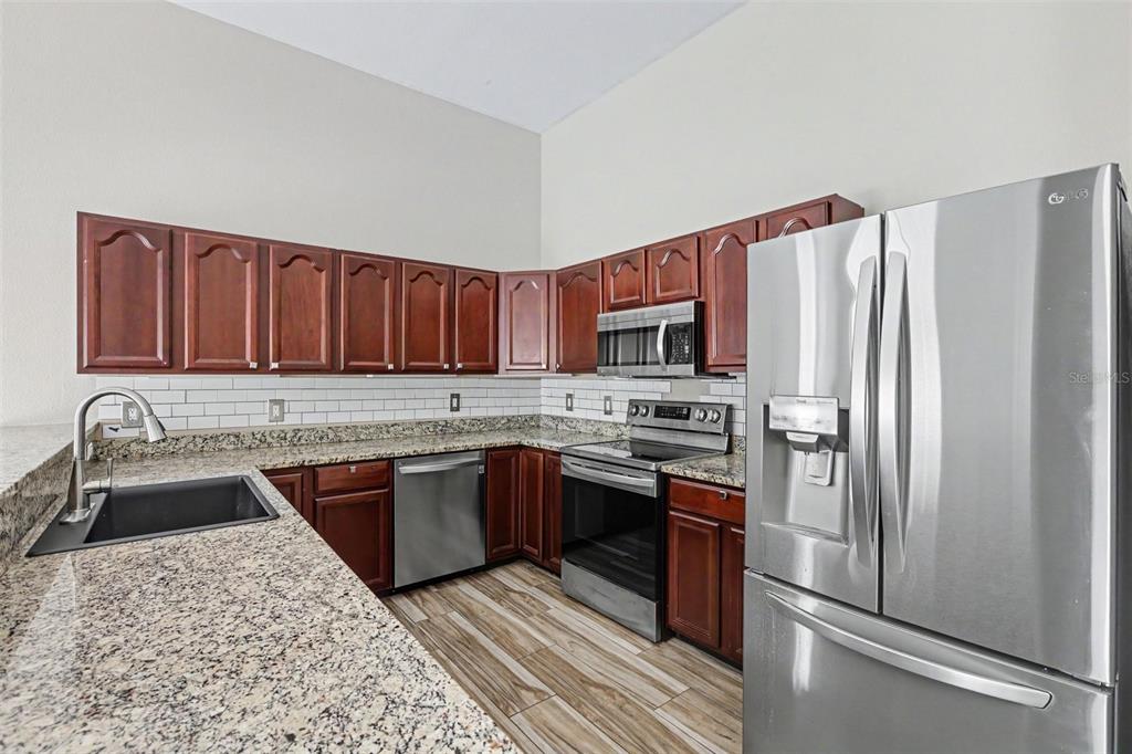 An open-concept living area features light wood-look flooring, a kitchen with dark cabinets, and stairs — 9548 ORANGE VALLEY COURT, TAMPA, FL