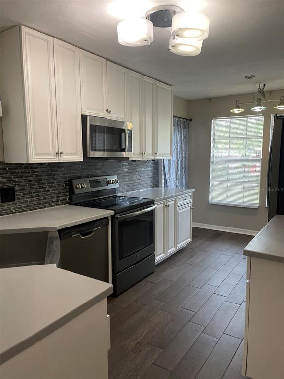 A kitchen features white cabinets, stainless steel appliances, a dark tile backsplash, and wood-look flooring — 245 ALSTON DRIVE, ORLANDO, FL