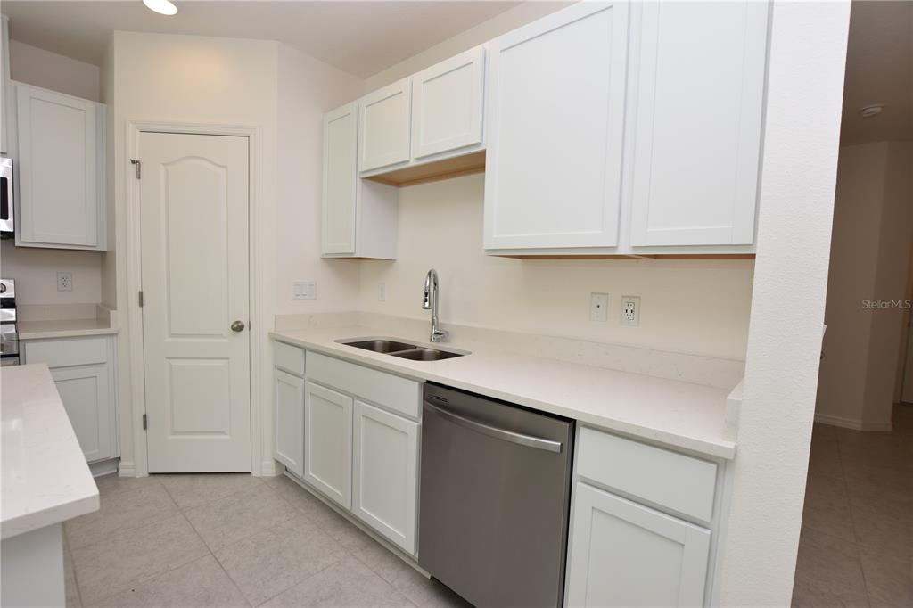 A kitchen with white cabinets, light countertops, a stainless steel dishwasher, and tile flooring — 3913 ACADEMIA AVENUE, LAKELAND, FL