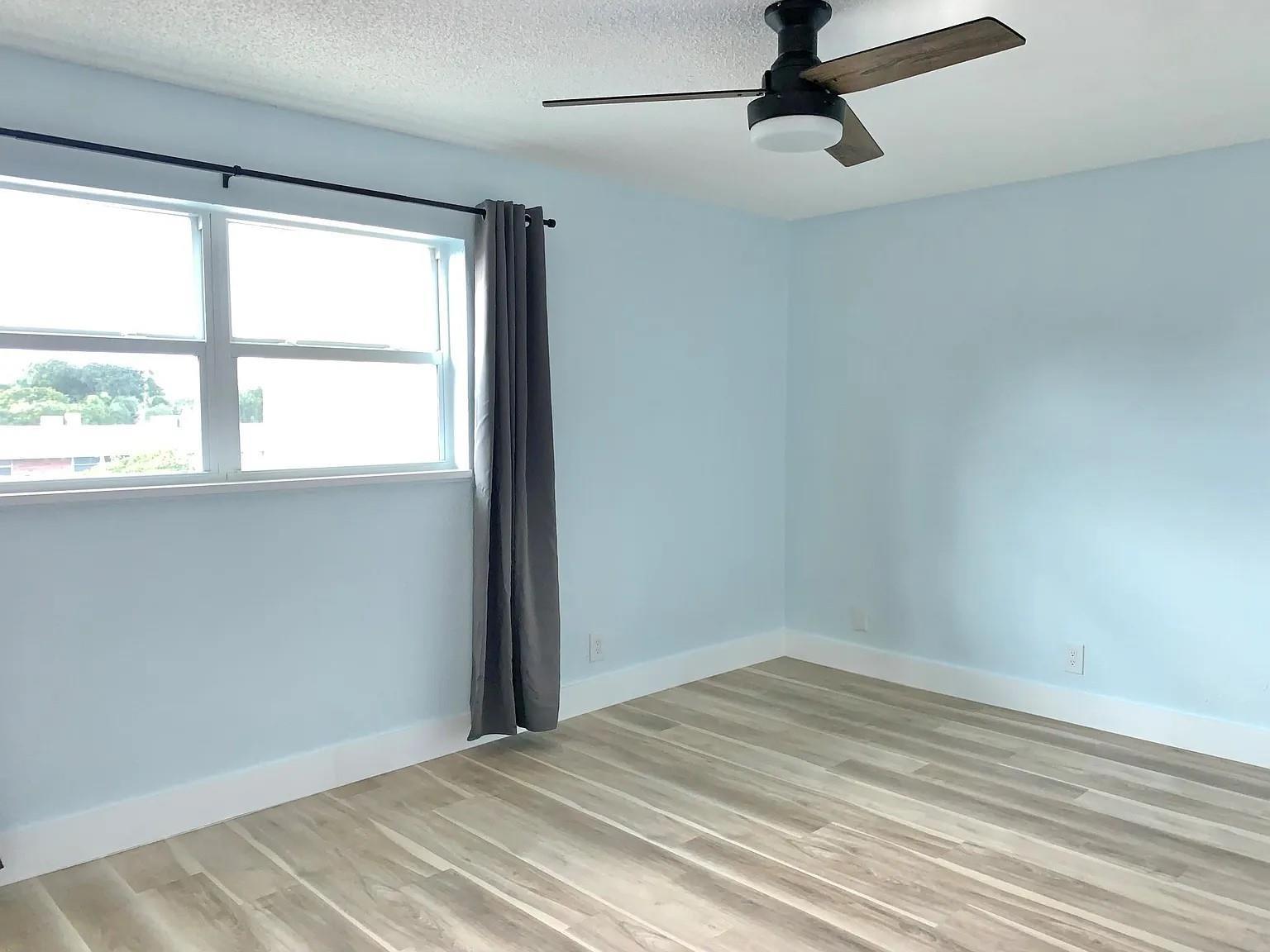 An empty bedroom with light blue walls, wood-look flooring, a ceiling fan, and a window — 2850 NE 14th Street # 306b, Pompano Beach FL 33062, POMPANO BEACH, FL