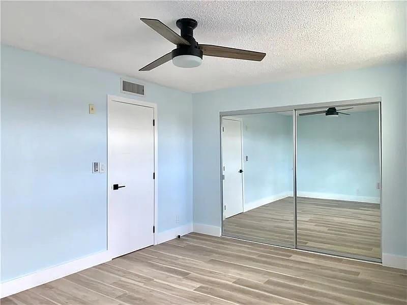 A bedroom with light blue walls, wood-look flooring, a ceiling fan, and mirrored closet doors — 2850 NE 14th Street # 306b, Pompano Beach FL 33062, POMPANO BEACH, FL
