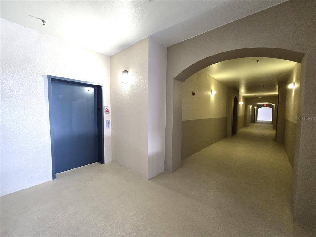 A hallway with a blue elevator door and arched architectural details leads to a distant exit — 3001 LAUREL RUN LANE UNIT 203, KISSIMMEE, FL