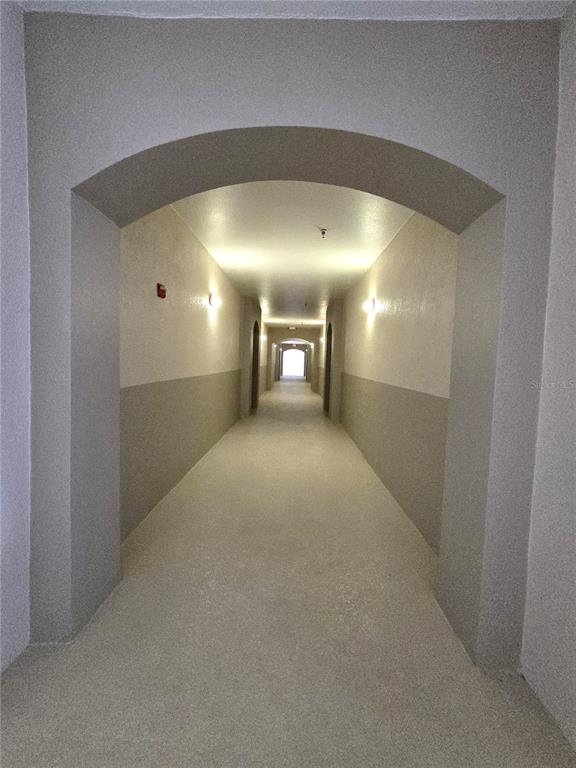 A long, empty apartment building hallway features arched entryways and neutral-toned walls — 3001 LAUREL RUN LANE UNIT 203, KISSIMMEE, FL