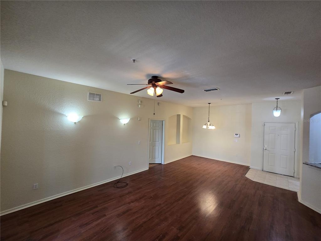 An open-concept living area features wood-look flooring, a ceiling fan, and wall-mounted light fixtures — 3001 LAUREL RUN LANE UNIT 203, KISSIMMEE, FL