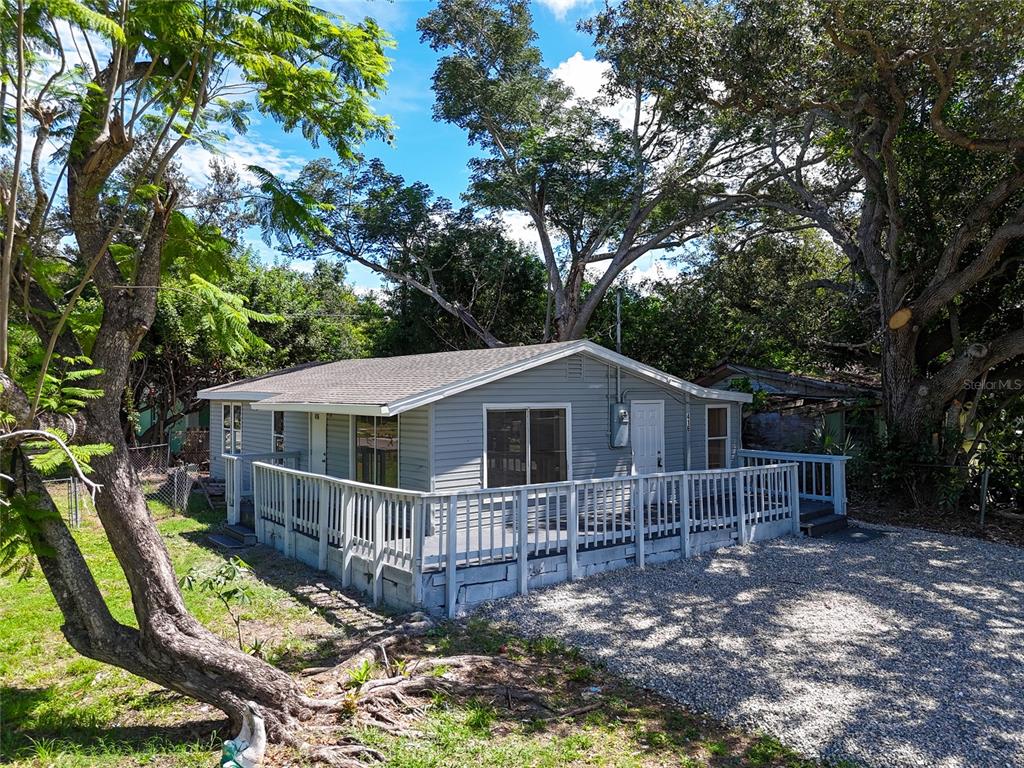 A small, grey, single-story house features a large wooden deck and a gravel driveway — 416 27TH AVENUE W, BRADENTON, FL