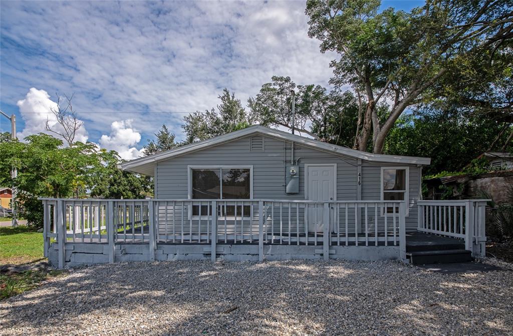 A gray, single-story house with a large wooden deck and gravel driveway under a cloudy sky — 416 27TH AVENUE W, BRADENTON, FL