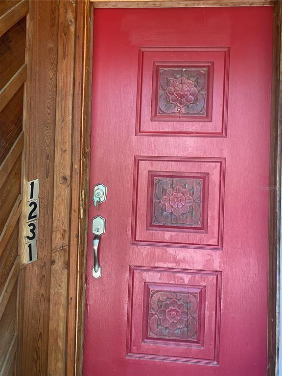 A red front door features three square carved floral panels and a silver handle set — 1231 NE 9TH STREET W, GAINESVILLE, FL