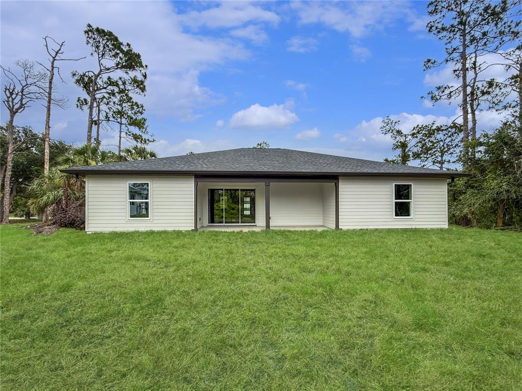 The rear exterior of a single-story house features light siding, a covered patio, and lawn — 73 BARSTOW STREET, PORT CHARLOTTE, FL