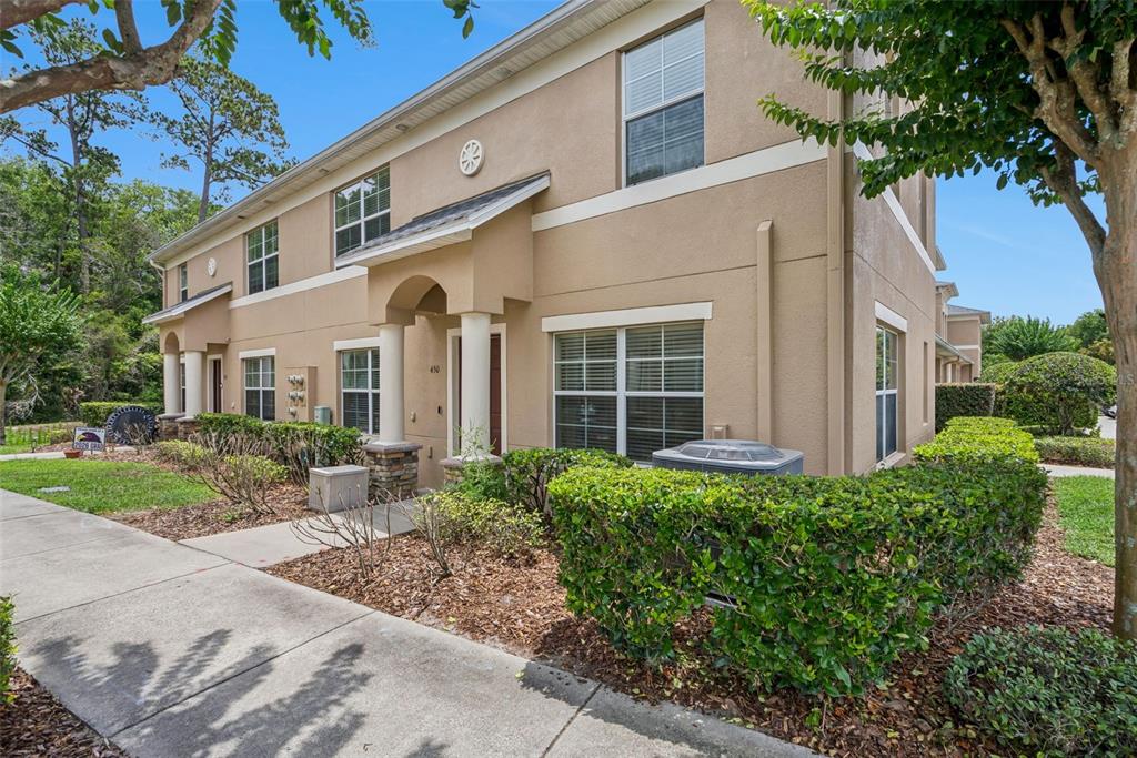 A two-story tan stucco townhouse features a covered entryway, white columns, and manicured hedges — 450 CARINA CIRCLE, SANFORD, FL