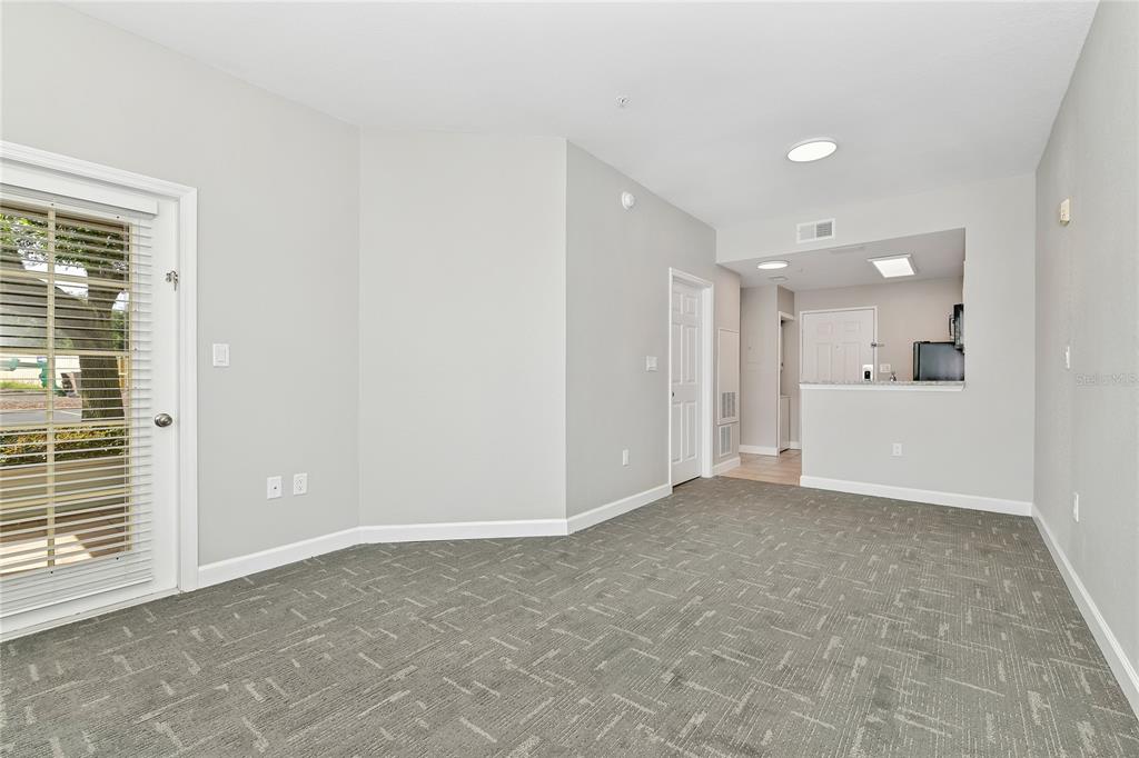 A living room with gray carpet, light walls, a glass door, and an open kitchen — 7503 ATLANTIS WAY UNIT J108, KISSIMMEE, FL