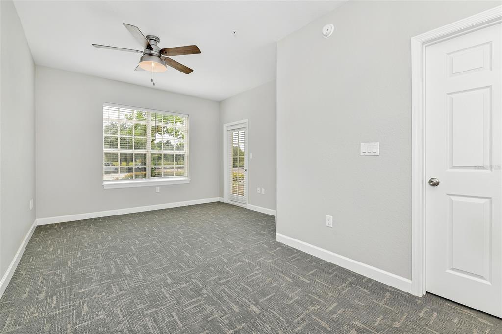 An empty room with gray carpet, light gray walls, a ceiling fan, and a door — 7503 ATLANTIS WAY UNIT J108, KISSIMMEE, FL