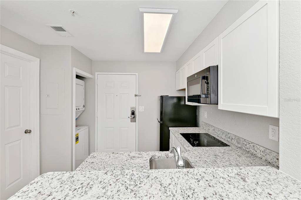 A kitchen features granite countertops, white cabinets, black appliances, and an adjacent laundry closet — 7503 ATLANTIS WAY UNIT J108, KISSIMMEE, FL