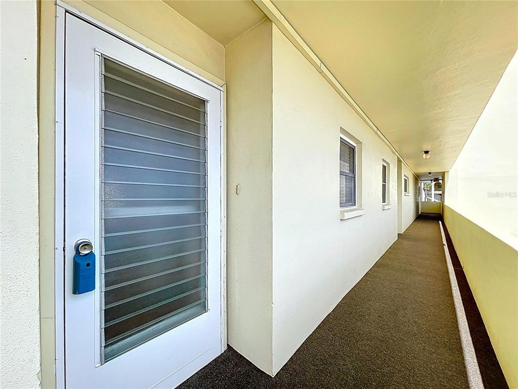 An exterior hallway with a white door and a blue lockbox on the left — 4650 COVE CIRCLE UNIT 209, ST PETERSBURG, FL
