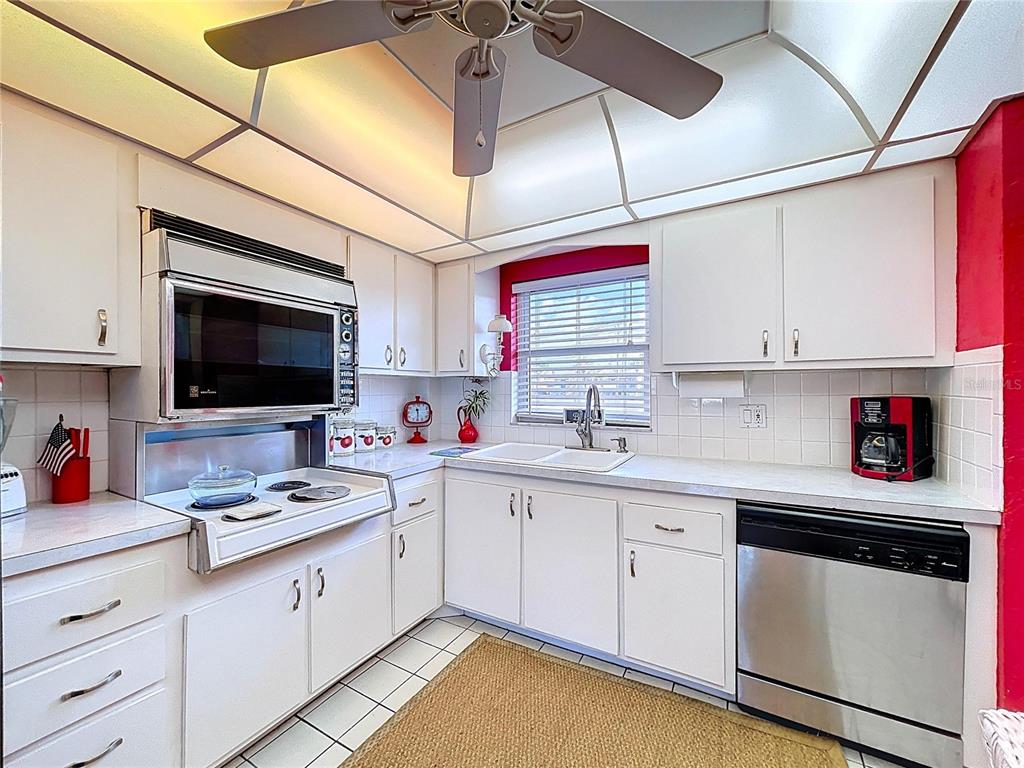 A kitchen features white cabinets, a stainless steel dishwasher, a drop-in stove, and tile flooring — 4650 COVE CIRCLE UNIT 209, ST PETERSBURG, FL