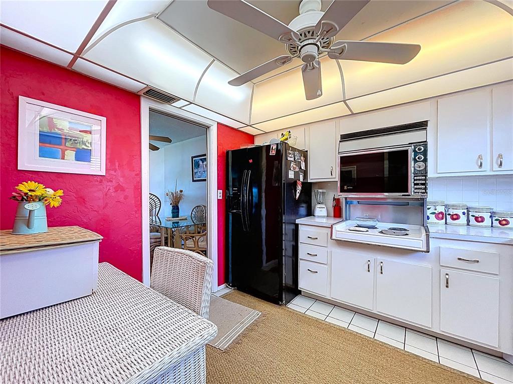 A kitchen features white cabinets, a black refrigerator, a ceiling fan, and a bright red wall — 4650 COVE CIRCLE UNIT 209, ST PETERSBURG, FL