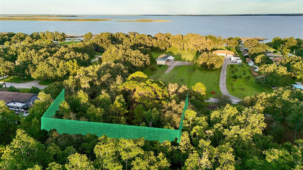 An aerial view shows a wooded lot marked by a green construction fence near water — 1514 BLACKWILLOW STREET, LAKE PLACID, FL