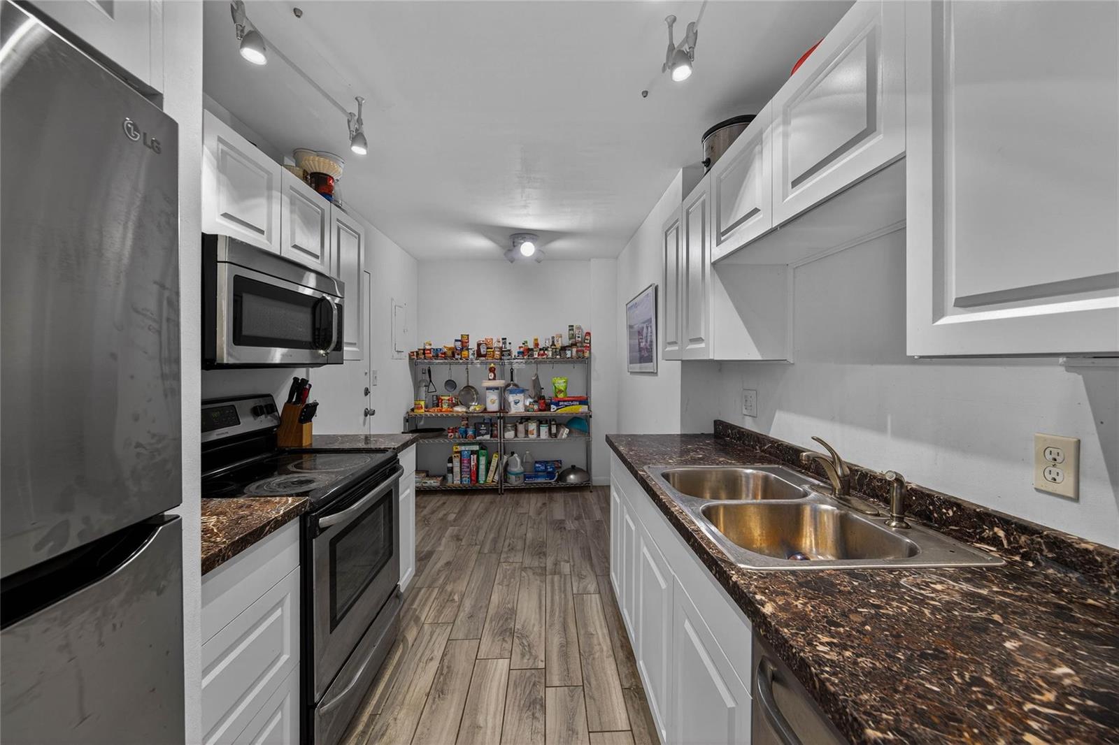 A galley kitchen features white cabinets, dark granite countertops, stainless steel appliances, and wood-look flooring — 4400 Hillcrest Drive # 704, Hollywood FL 33021, HOLLYWOOD, FL