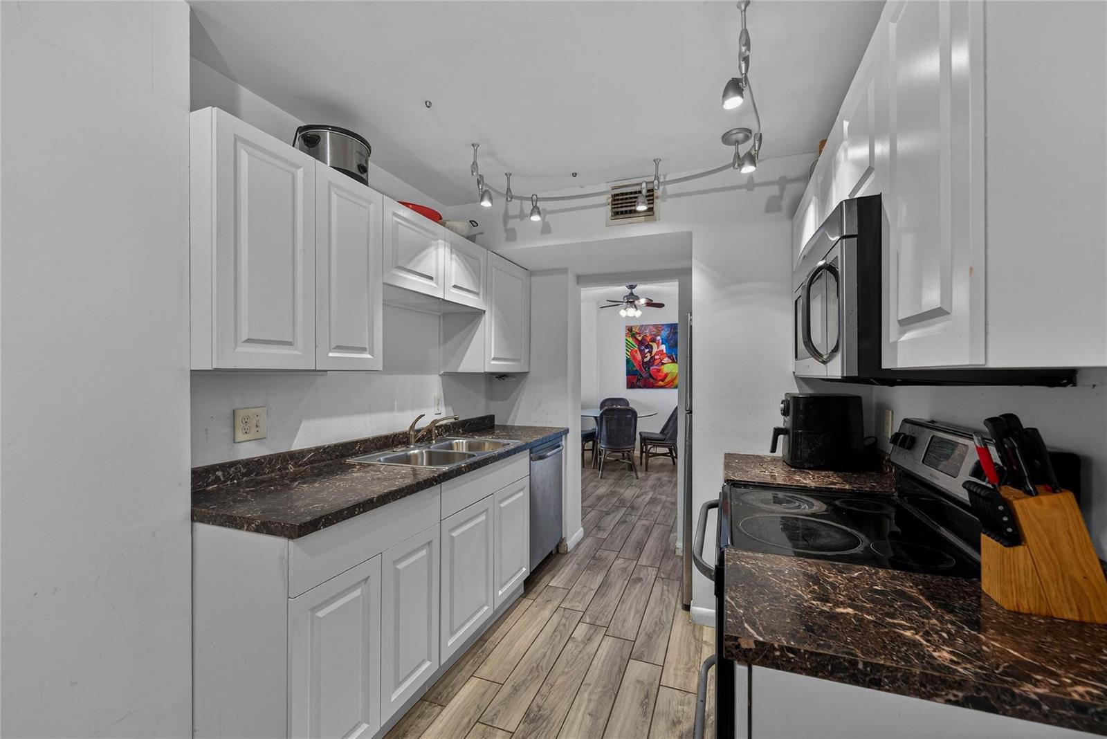 A galley kitchen features white cabinets, dark marble-look countertops, and stainless steel appliances — 4400 Hillcrest Drive # 704, Hollywood FL 33021, HOLLYWOOD, FL