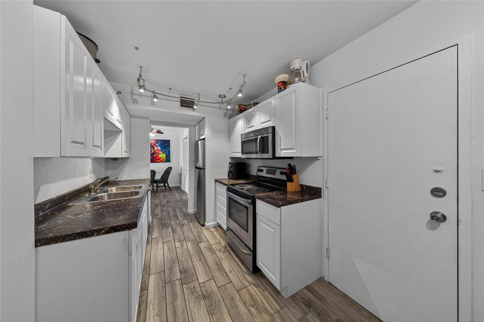 A galley kitchen features white cabinets, dark countertops, stainless steel appliances, and wood-look flooring — 4400 Hillcrest Drive # 704, Hollywood FL 33021, HOLLYWOOD, FL