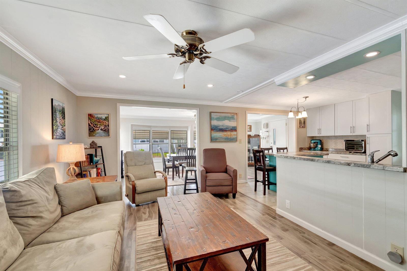 A living room with a ceiling fan, wood coffee table, and an open kitchen area — 14001 Kingston Bay, Boynton Beach FL 33436, BOYNTON BEACH, FL