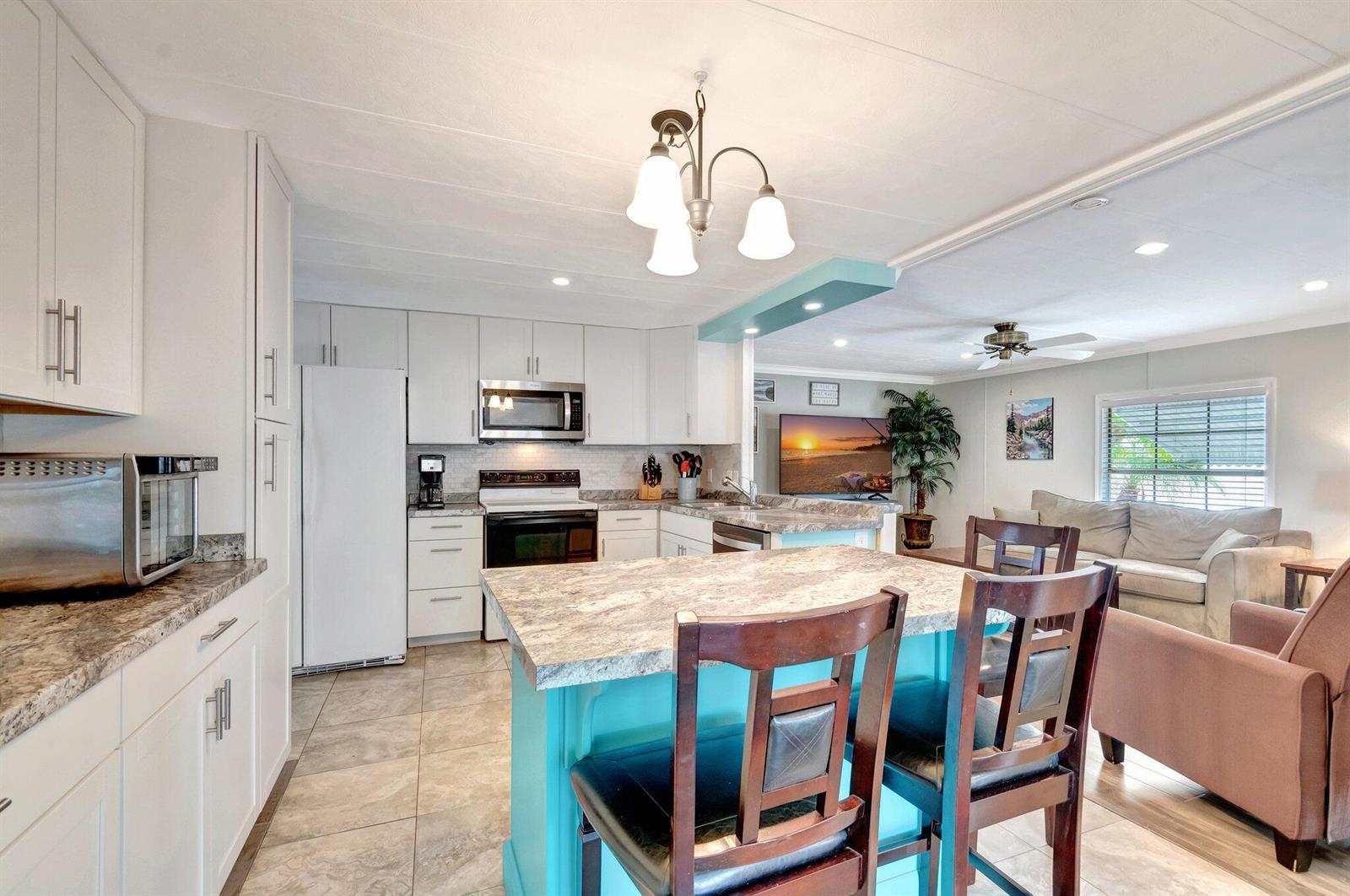 A kitchen with white cabinets, a teal island, and a dining area in an open-concept home — 14001 Kingston Bay, Boynton Beach FL 33436, BOYNTON BEACH, FL