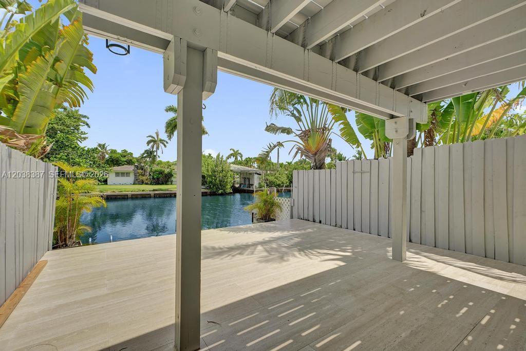 A covered wooden deck overlooks a canal with tropical landscaping and a privacy fence — 2129 NE 123rd St # 0, North Miami FL 33181, NORTH MIAMI, FL