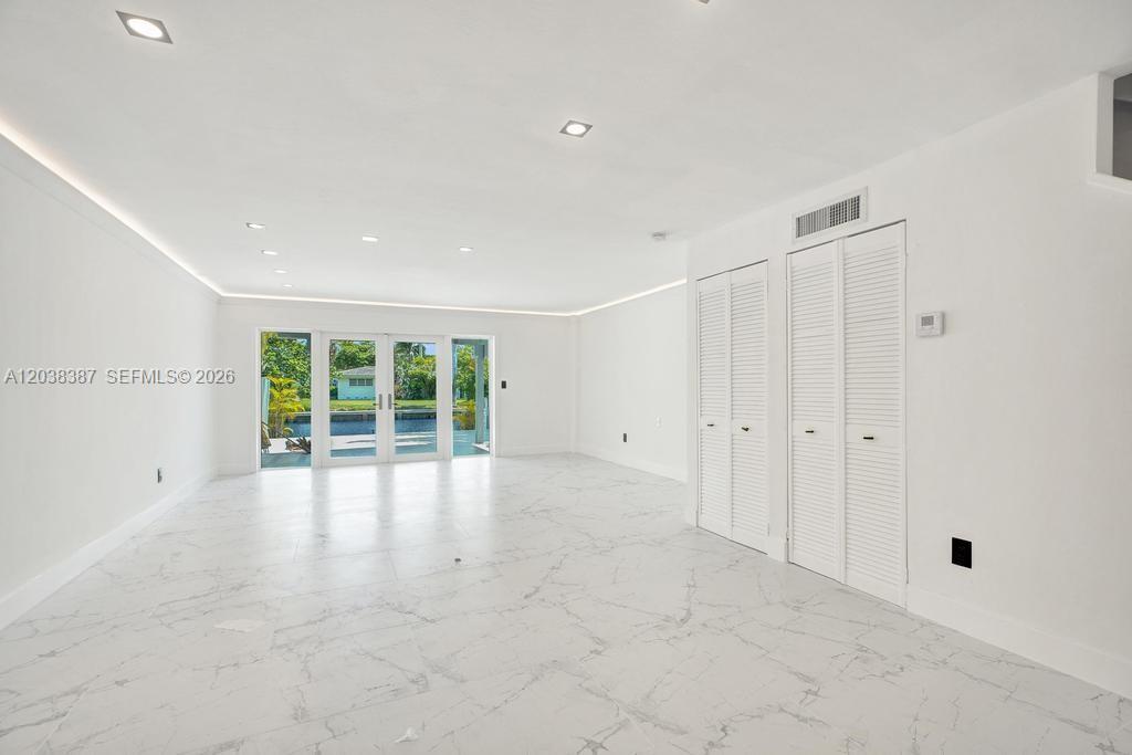 A bright, empty room features white marble flooring, recessed lighting, and glass doors overlooking water — 2129 NE 123rd St # 0, North Miami FL 33181, NORTH MIAMI, FL