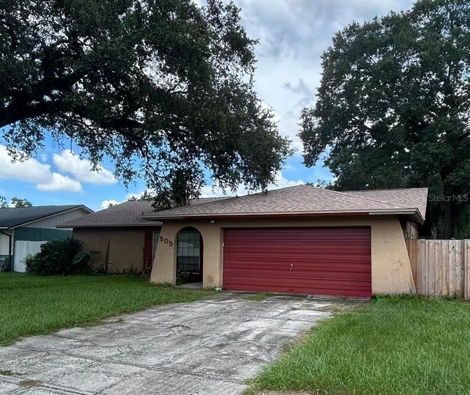 A single-story house with a red garage door, tan stucco siding, and a concrete driveway — 505 PROCLAMATION DRIVE, TAMPA, FL