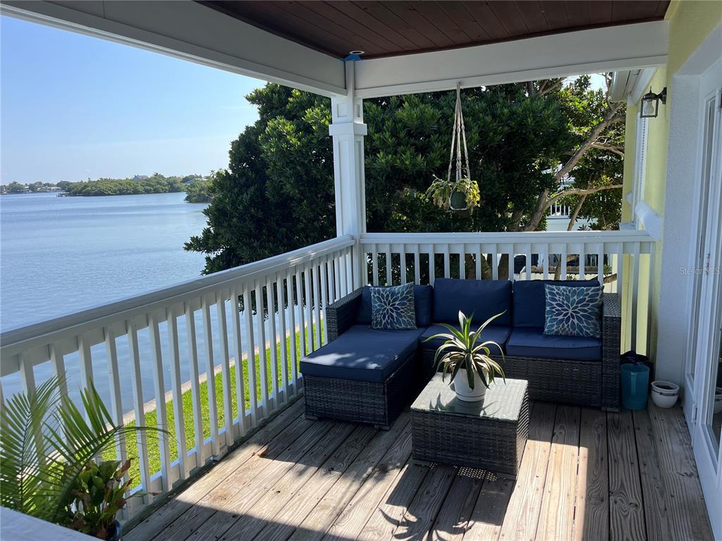 A covered wooden deck overlooks a body of water with a sectional sofa and table — 205 POMPANO DRIVE SE UNIT D, ST PETERSBURG, FL