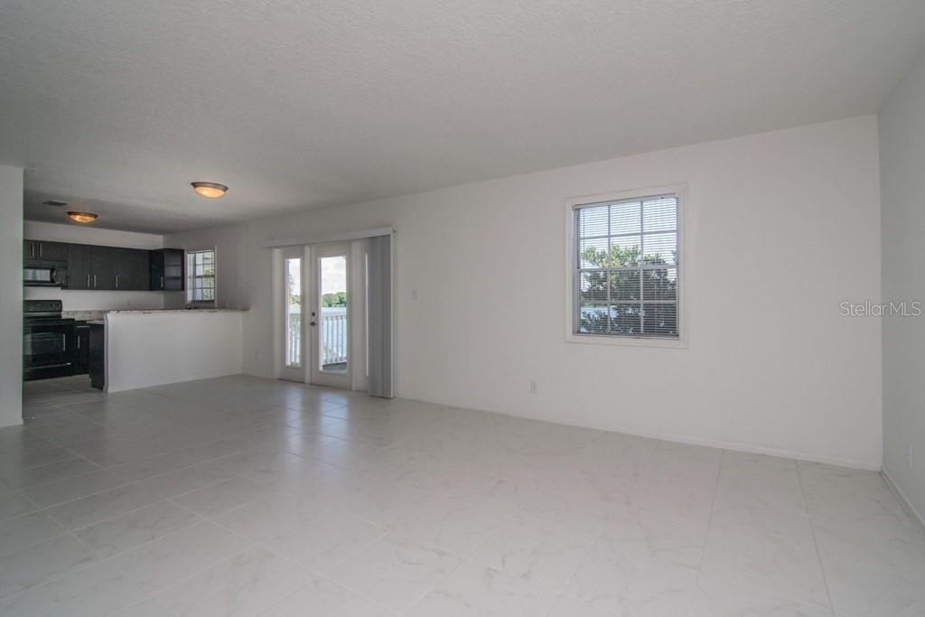 An open-concept living area features white tile flooring, a kitchen with dark cabinets, and sliding doors — 205 POMPANO DRIVE SE UNIT D, ST PETERSBURG, FL