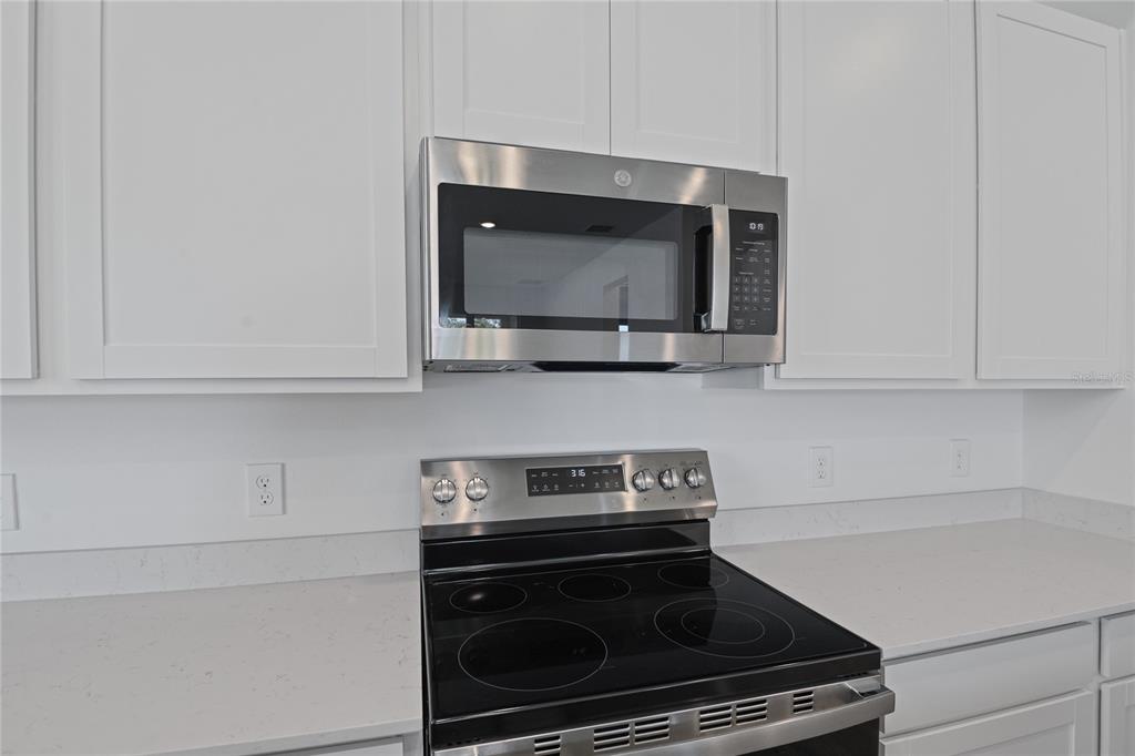 A stainless steel microwave and electric range are installed between white cabinets and countertops — 746 LAKE DELL AVENUE, DUNDEE, FL