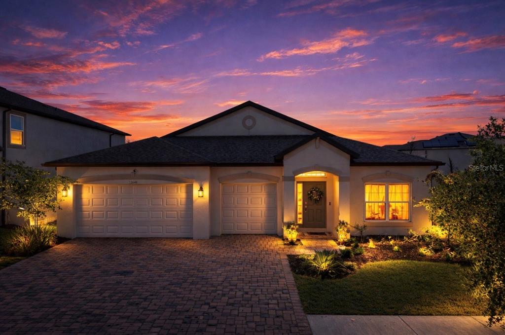 A single-story house with a two-car garage and a paved driveway at sunset — 12048 ORCHID ASH STREET, RIVERVIEW, FL