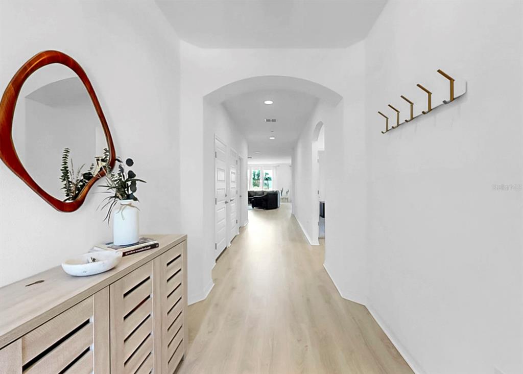 A bright hallway features light wood flooring, a console table with a mirror, and wall hooks — 12048 ORCHID ASH STREET, RIVERVIEW, FL