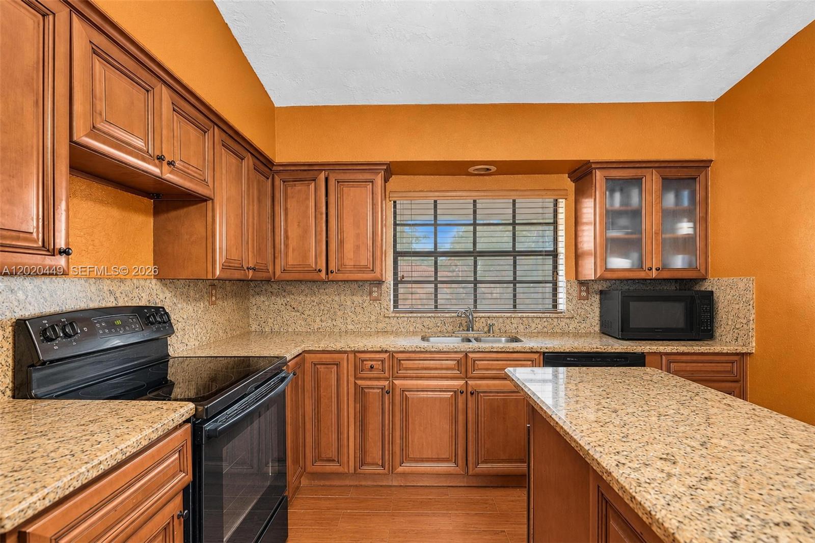 A kitchen features wood cabinets, granite countertops, a black stove, and orange walls — 11061 SW 163rd St, Miami FL 33157, MIAMI, FL
